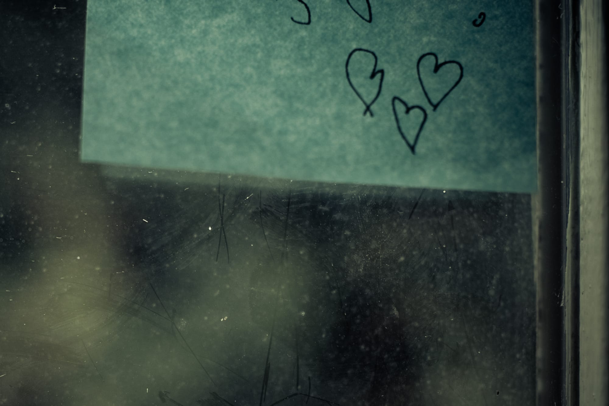 Ein an ein Fenster geklebtes Post-It, das drei Herzen zeigt.