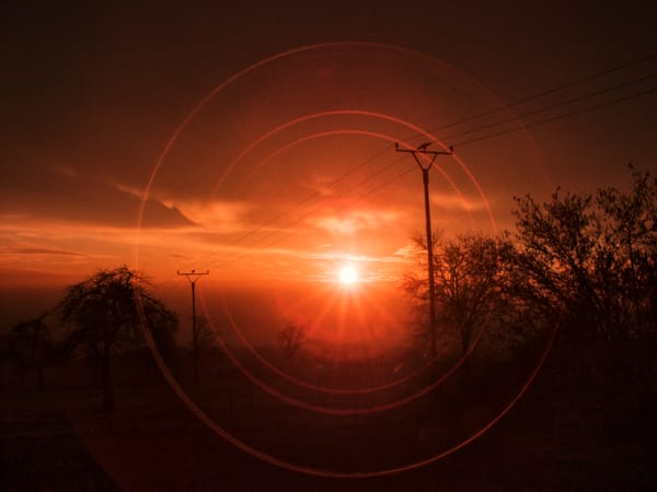 Ein Sonnenuntergang mit Strommasten im Vordergrund. Die Sonne bildet Reflektionen im aufnehmenden Objektiv.