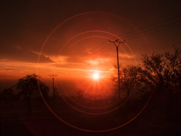 Ein Sonnenuntergang mit Strommasten im Vordergrund. Die Sonne bildet Reflektionen im aufnehmenden Objektiv.