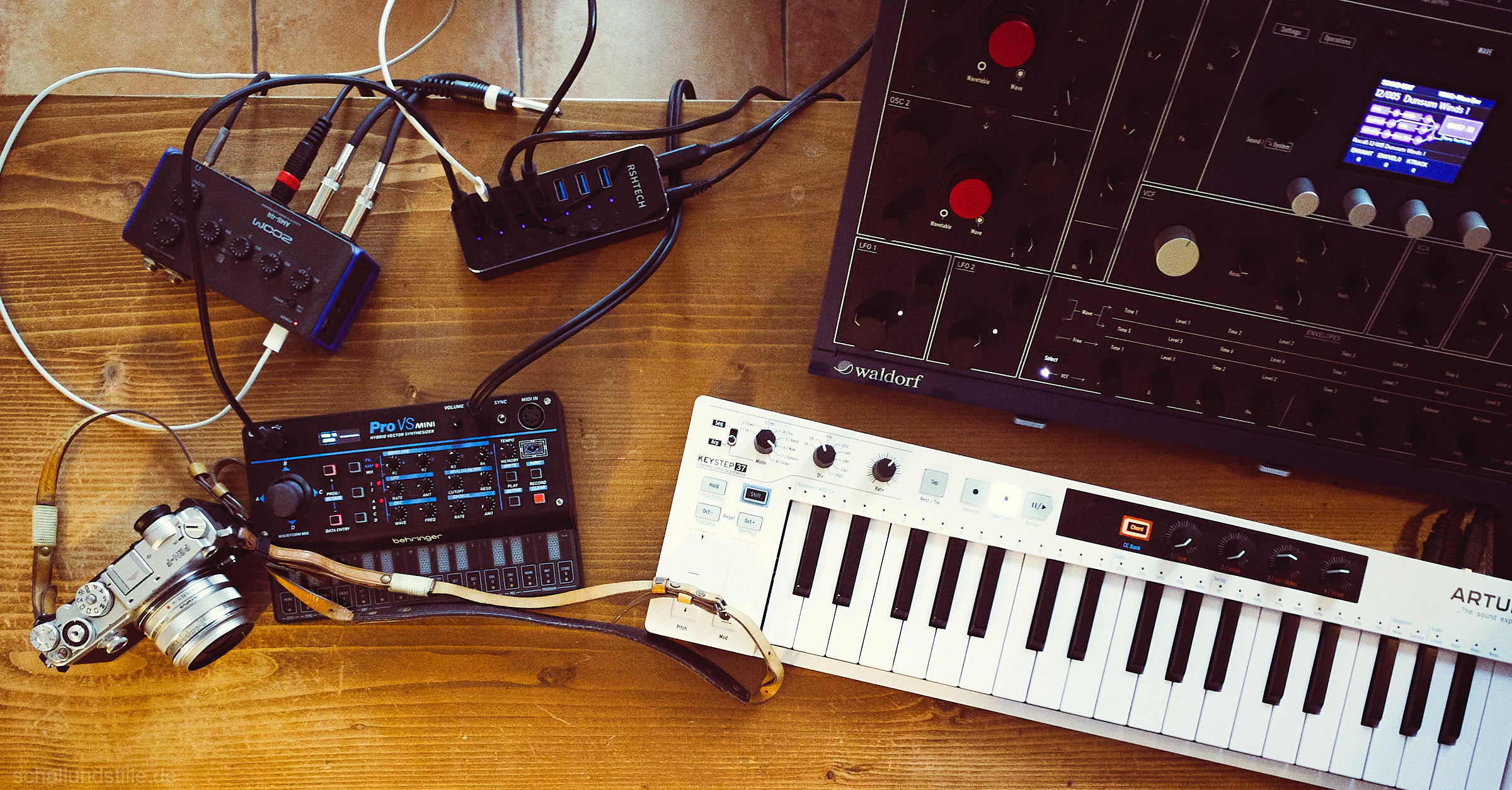 an Olympus Pen F, a Behringer Pro VS Mini, an Arturia keystep and a Waldorf M on a wooden table