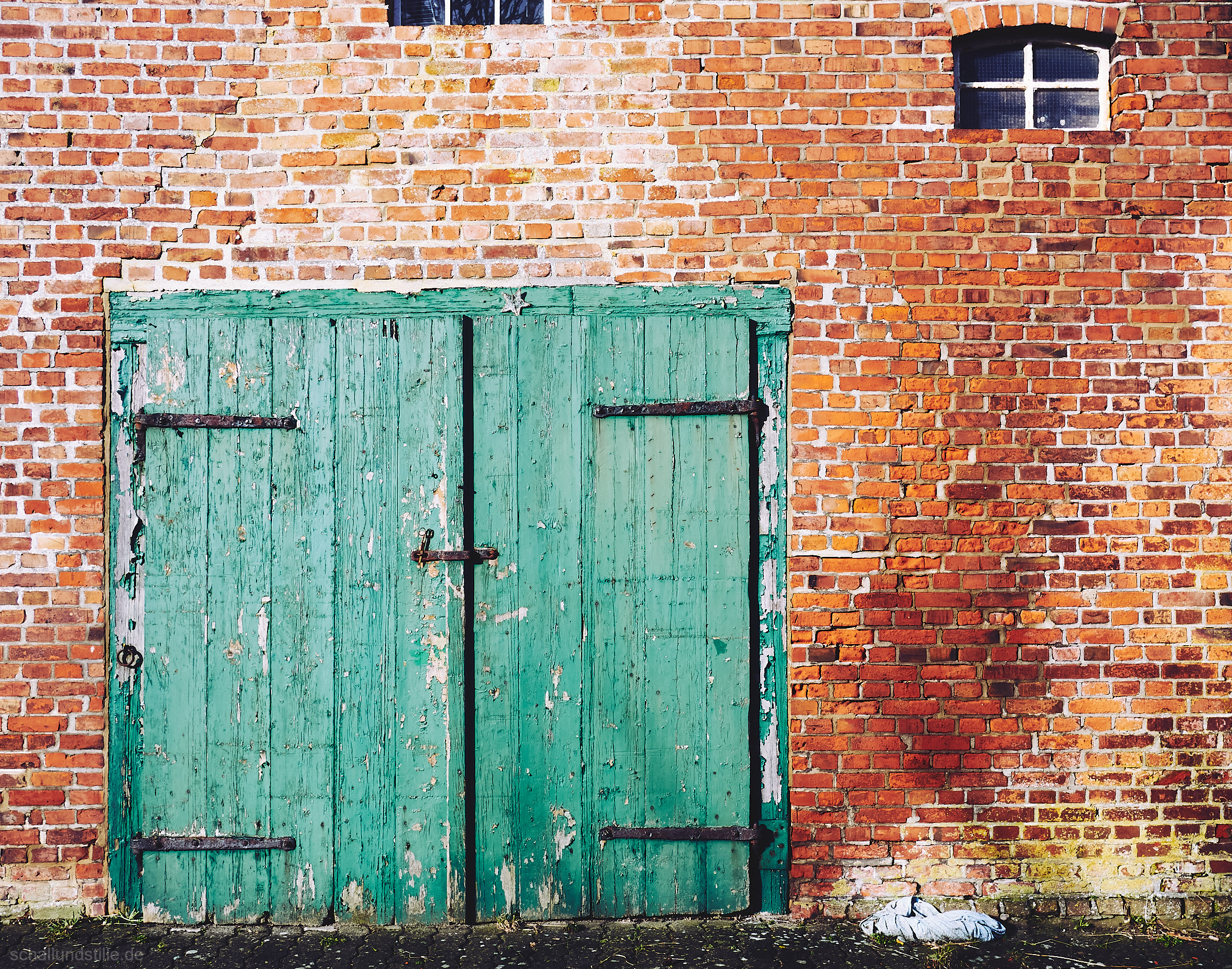 a turquoise barn door in a red brick wall