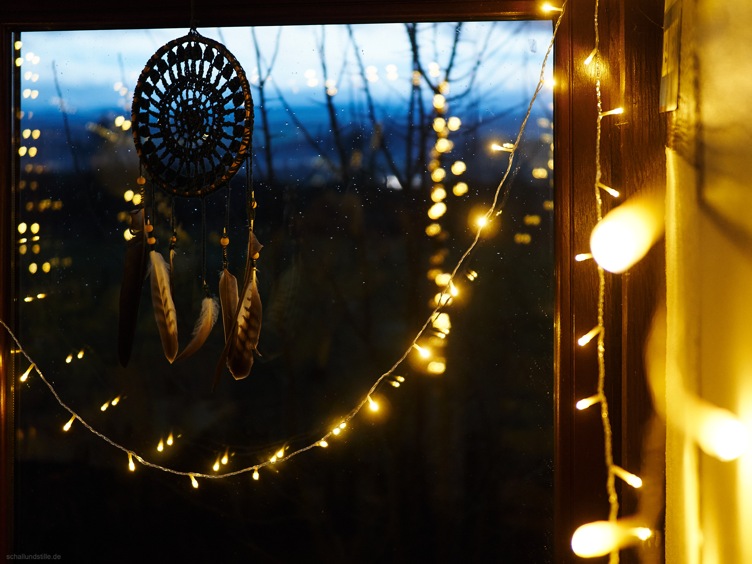 fairy lights and a dream catcher before a window, outside a dark evening scene