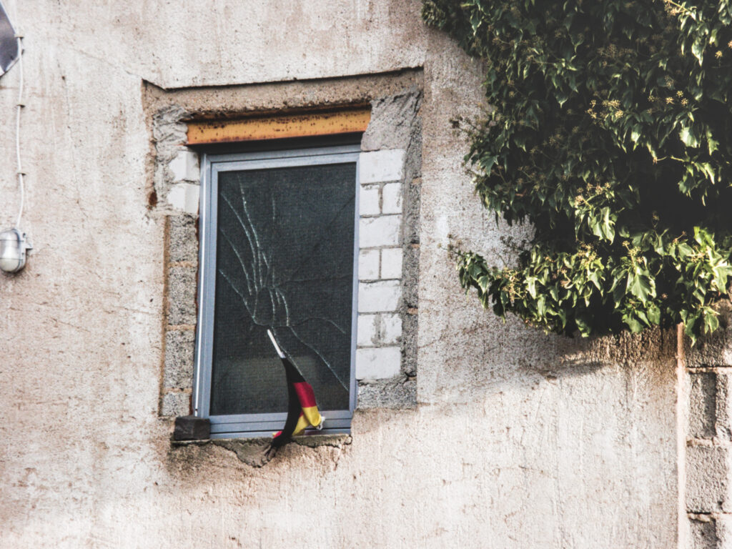 A derelict building with an equally derelict German flag and some ivy on the right. 