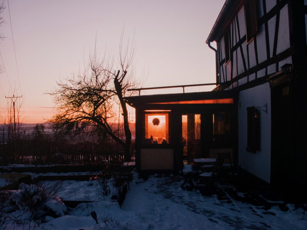 The sun going down behind a winter garden adjacent to a cottage. 