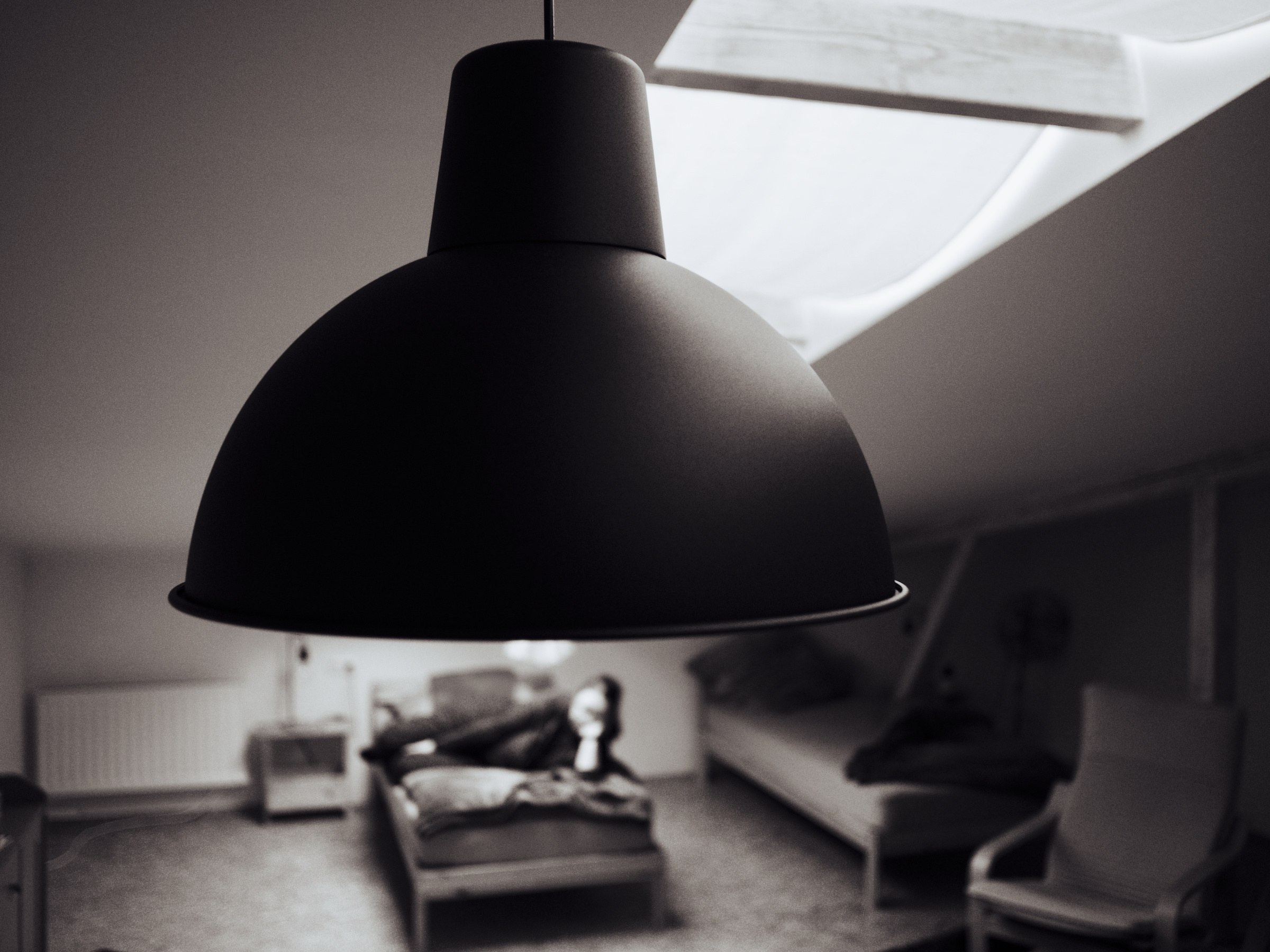 closeup of a lamp in a loft, in the background a single bed with a person on it