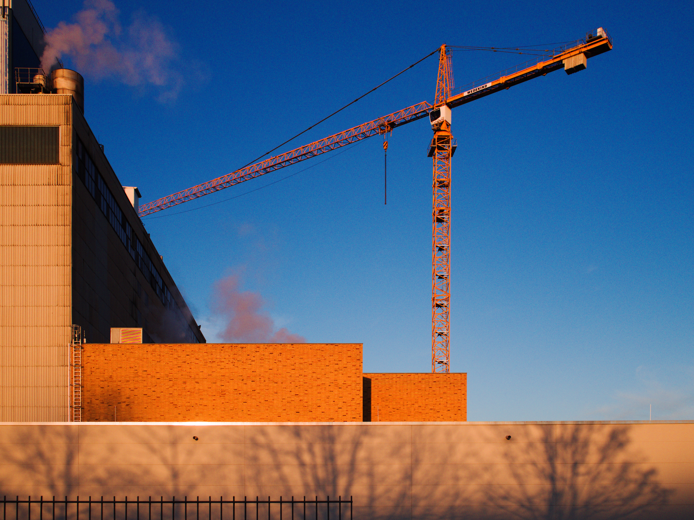 part of an industrial building with a red crane against a blue evening sky